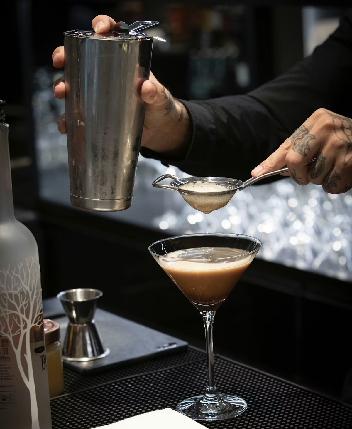 Bartender straining a craft cocktail into a martini glass — maximalism bar trend 2026